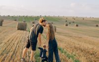 A couple with their child enjoy a sunny day in a wheat field, symbolizing love and joy.
